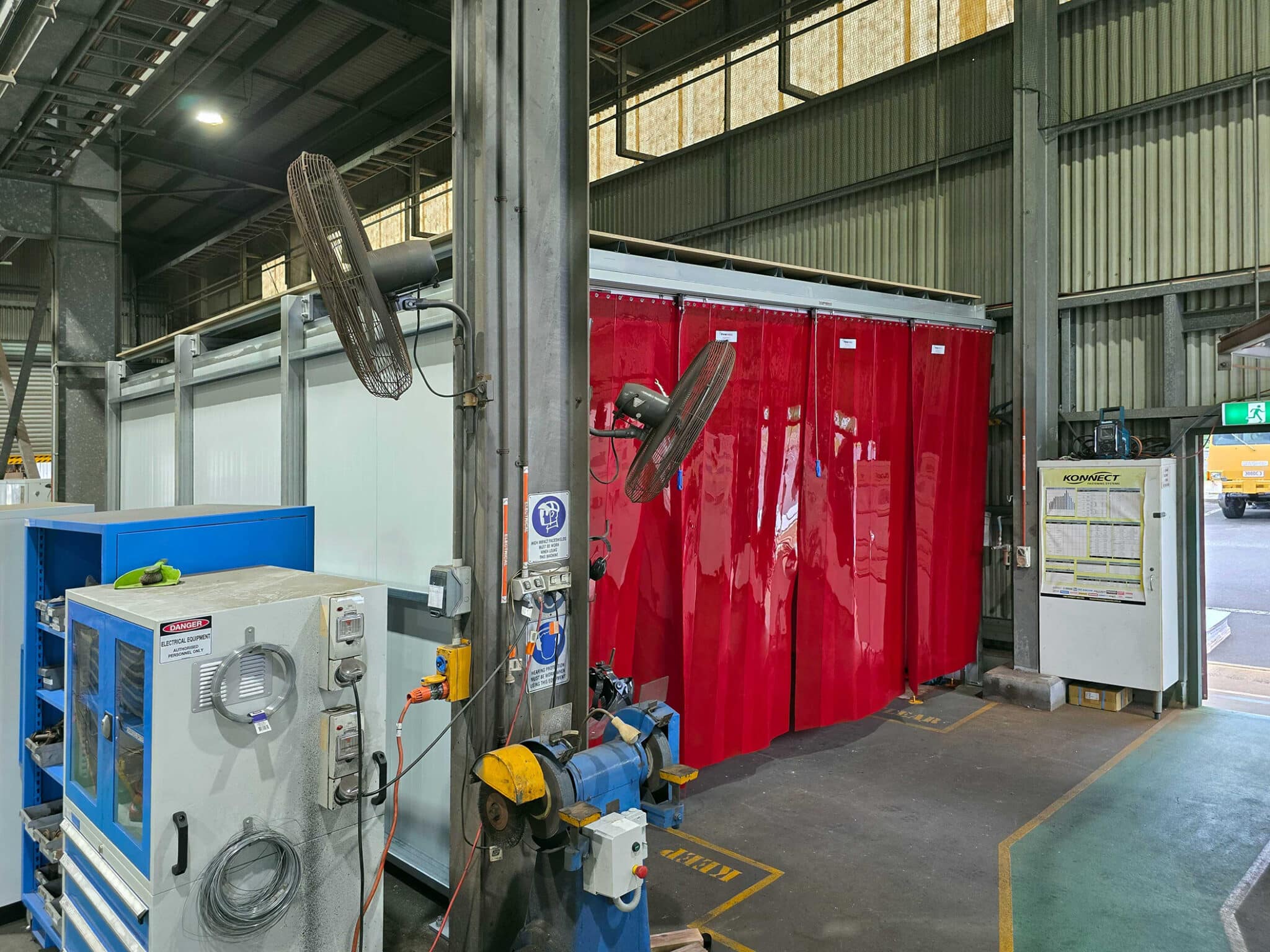 Sonic System acoustic modular panels forming the walls of a welding bay, with red Weldflex™ strip curtains across the front inside a Queensland Rail workshop.