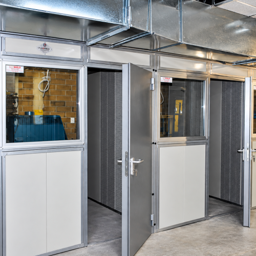 Flexshield enclosed acoustic work bays with glazed doors, modular acoustic panels and overhead ventilation ducting.