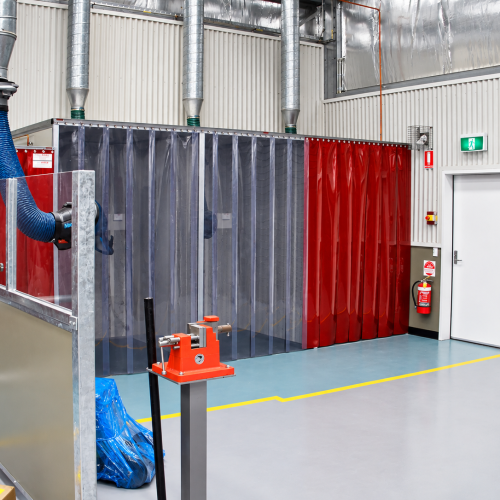 Flexshield welding and grinding bay with Weldflex™ strip curtains and overhead fume extraction in an industrial workshop.