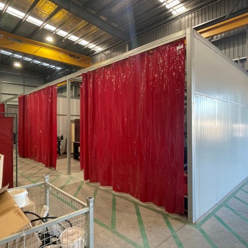 Flexshield acoustic welding bays with Sonic System acoustic modular panel walls and red Weldflex™ strip curtains inside an industrial workshop.