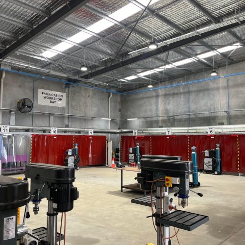 Multiple Flexshield acoustic welding bays with red Weldflex™ strip curtains and overhead extraction in a fabrication workshop.