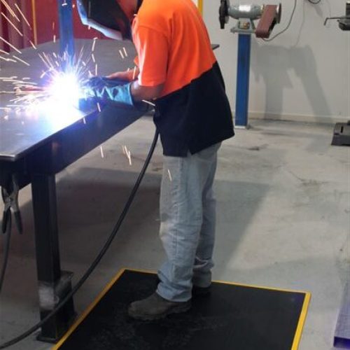 Welding operator standing on a FlexWeld floor mat while welding at a workbench