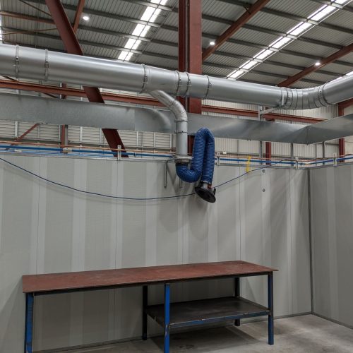 Flexible welding fume extraction arm connected to overhead ducting above an industrial workshop bench