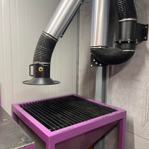 Close-up of adjustable welding fume extraction arms and hoods above an industrial work area