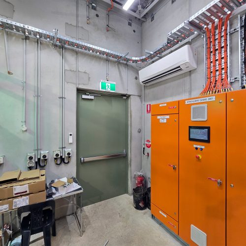 Green Sonic Access acoustic door installed beside electrical control cabinets inside an industrial plant room.