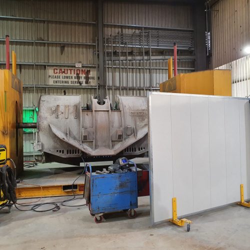 White Sonic System mobile acoustic panel on yellow castor supports positioned beside large mining equipment in a maintenance workshop.