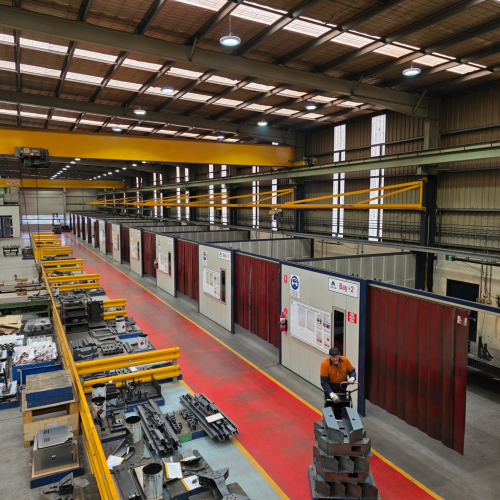 Multiple Flexshield acoustic welding bays with Weldflex strip curtains positioned alongside fabrication workstations in a large workshop.