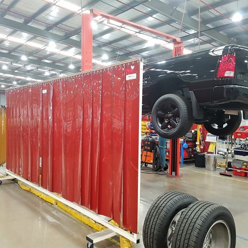 Weldflex™ mobile screen with red welding strips beside a vehicle hoist