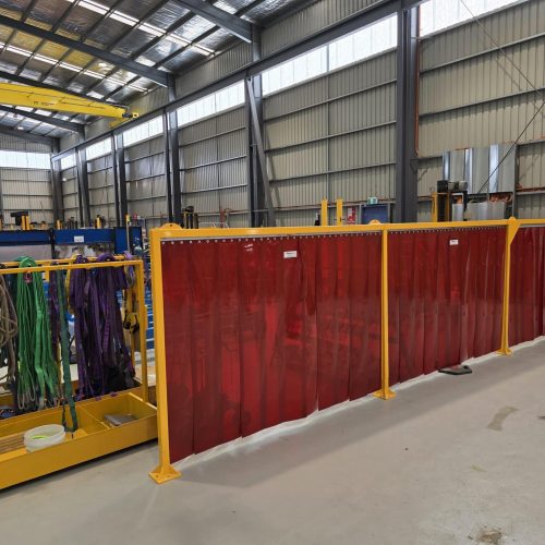 Red Weldflex™ Strip Curtains mounted on yellow frames to separate a work area inside an industrial workshop.