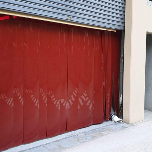 Red Weldflex™ Strip Curtains hanging across a roller door opening at an industrial premises.