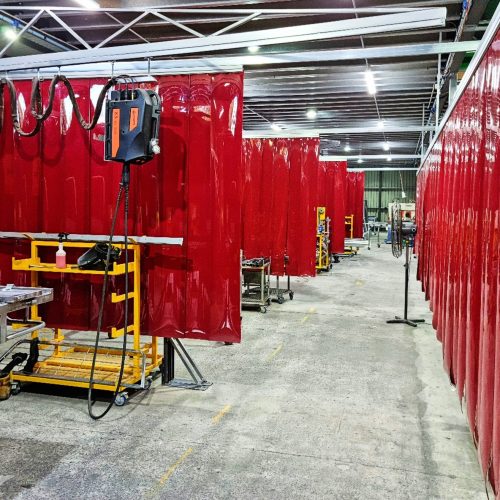 Red Weldflex™ Strip Curtains dividing multiple welding workstations inside a fabrication workshop.