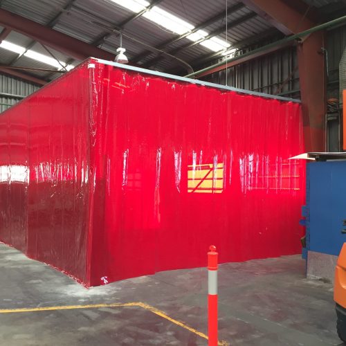 Red Weldflex™ sheet curtains forming a large enclosed work area inside an industrial workshop.