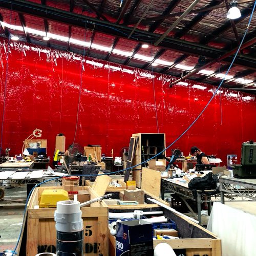 Large red Weldflex™ sheet curtains separating work areas inside a busy industrial workshop.