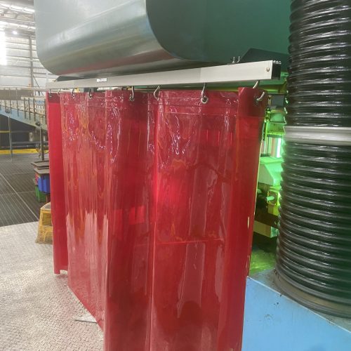 Red Weldflex™ sheet curtains suspended around industrial machinery beside large extraction ducting.