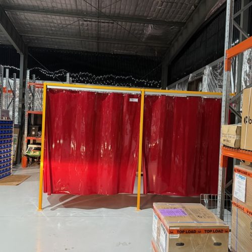 Red Weldflex™ sheet curtains mounted on a yellow freestanding frame inside an industrial warehouse.
