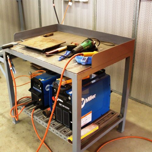 Flexshield Welding tables with steel work surface, raised sides and lower equipment shelf in an industrial workshop