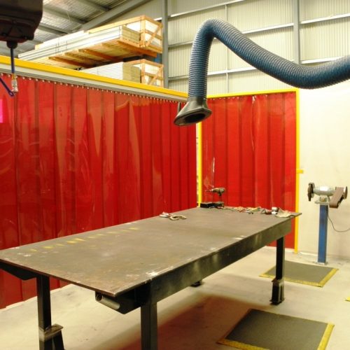 Large Flexshield Welding tables with overhead extraction arm and Weldflex™ welding strip curtains in an industrial workshop